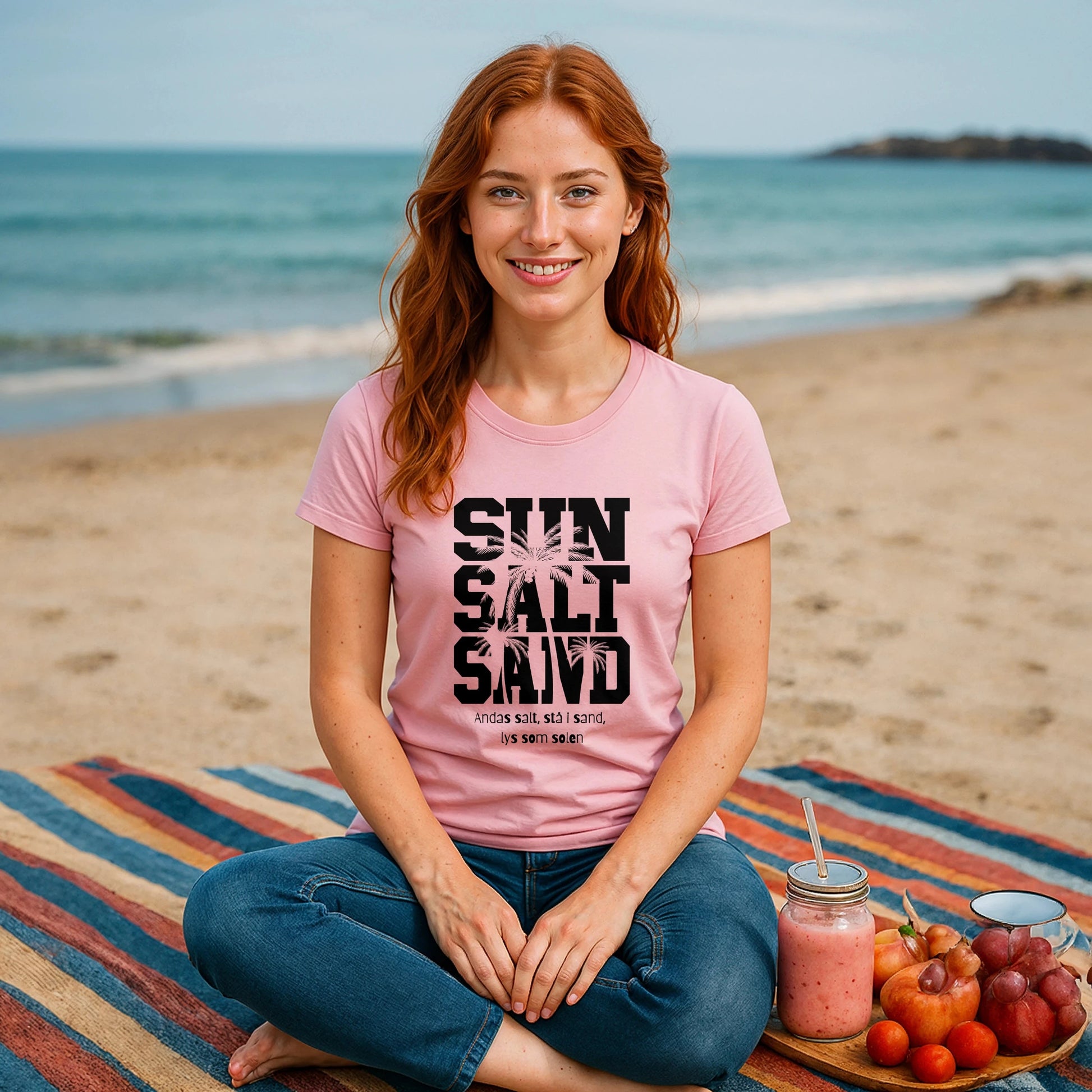 Sol Salt Sand 100% Organic Cotton T-Shirt pink graphic tee on woman sitting on beach blanket with ocean backdrop