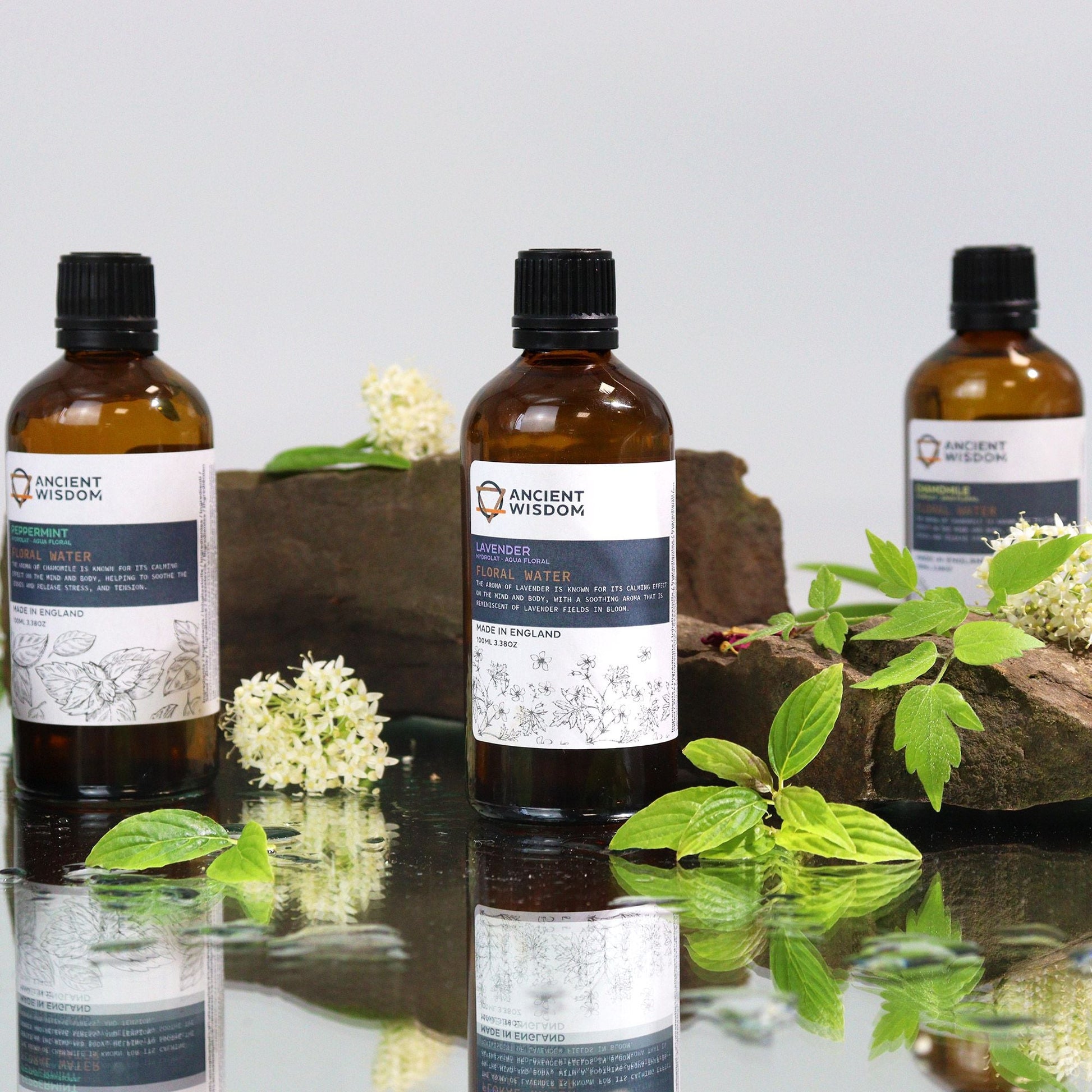 Soothing Chamomile Hydrolat – 100ML spray bottle product photo on reflective surface with green leaves and flowers