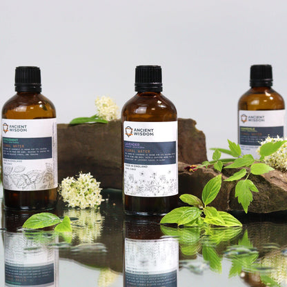 Soothing Chamomile Hydrolat – 100ML spray bottle product photo on reflective surface with green leaves and flowers