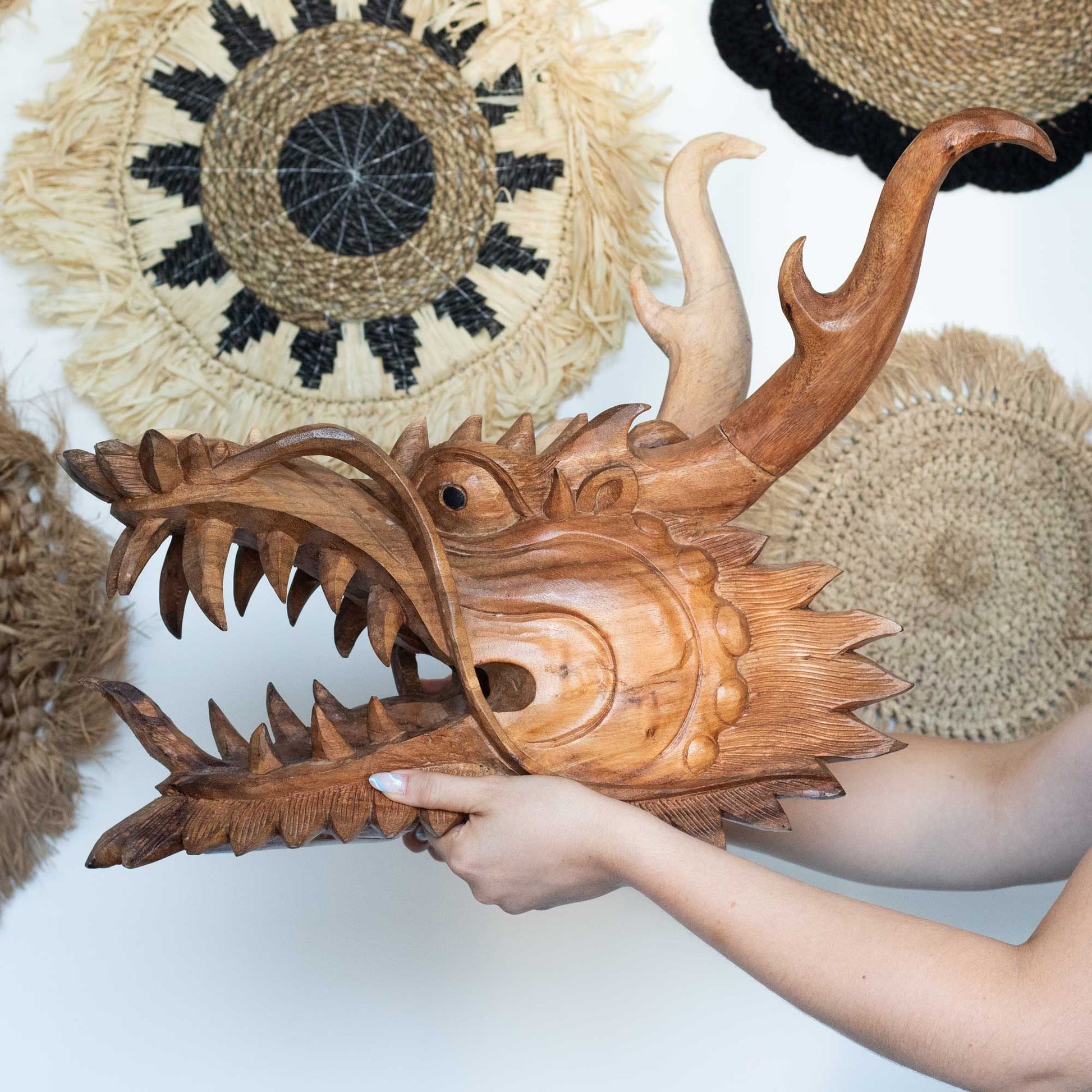 Alt Tag: Suar Wood Dragon Head Panel – 30 CM hand-carved wooden dragon head wall decor, held in hands with woven wall baskets backdrop