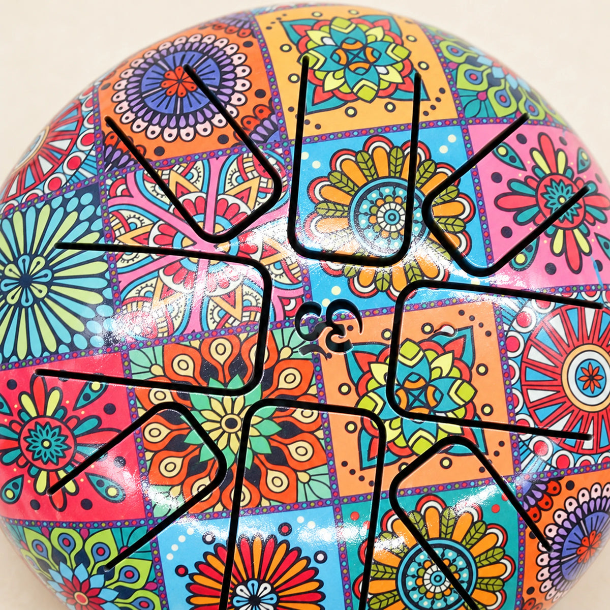 Close view of curved tongue slots and the small central cutout on the drum's colourful printed playing surface.
