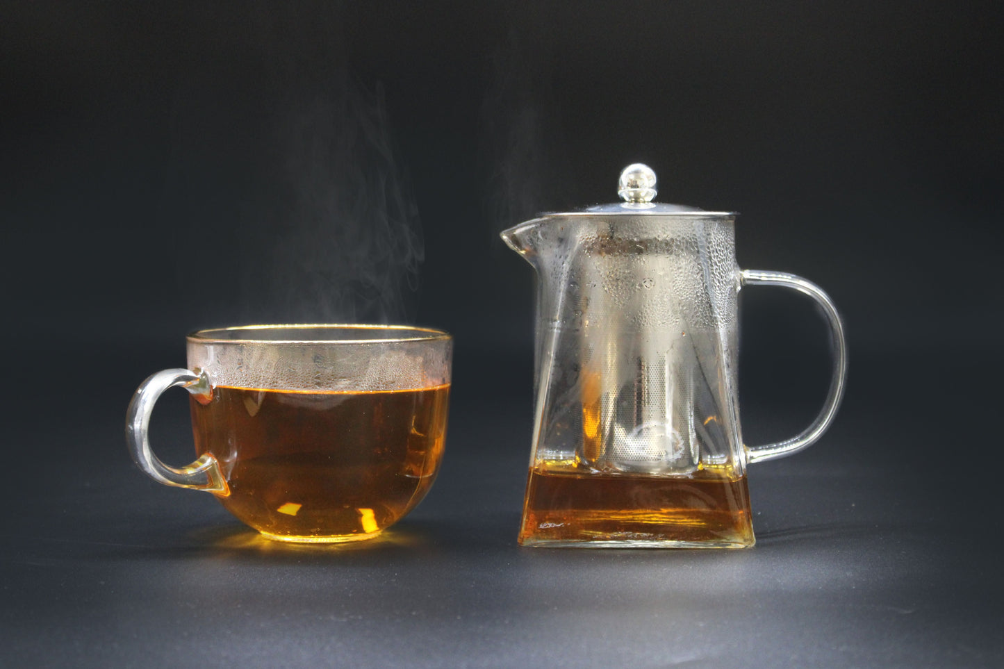 Tower Shape Glass Infuser Teapot – 750ML with stainless steel infuser, clear glass teapot and cup with brewed tea on dark background