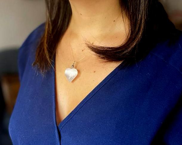 Translucent Selenite Heart Pendant – 4x2.5 CM worn on necklace, heart-shaped selenite charm on model in blue V-neck top