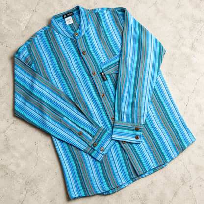 Turquoise and blue striped Nomad Sari shirt laid flat on a pale surface, showing its band collar, crossed sleeves and curved hem.