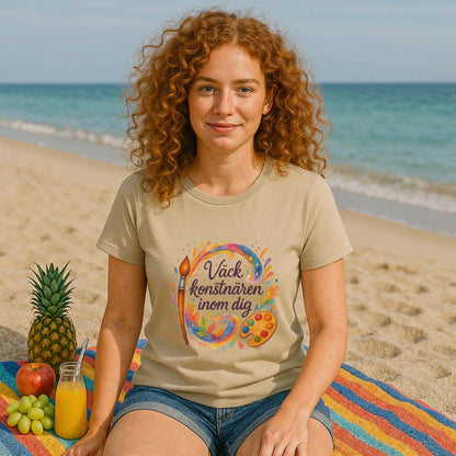 Alt Tag: Väck Konstnären Inom Dig Waldorf Sustainable Unisex Tee på kvinna på stranden, beige t-shirt med färgglad konstdesign och text