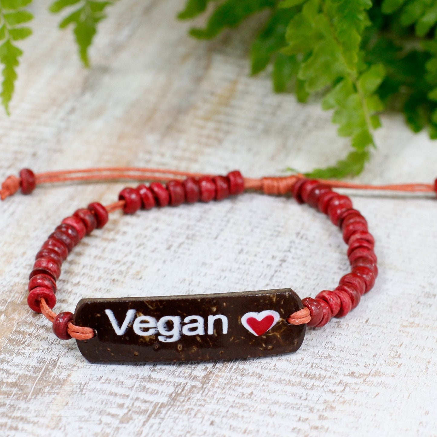 Alt Tag: Vegan Coconut Bead Stretch Bracelet – 7.5 CM red coconut bead cord bracelet with “Vegan” tag on rustic wood background