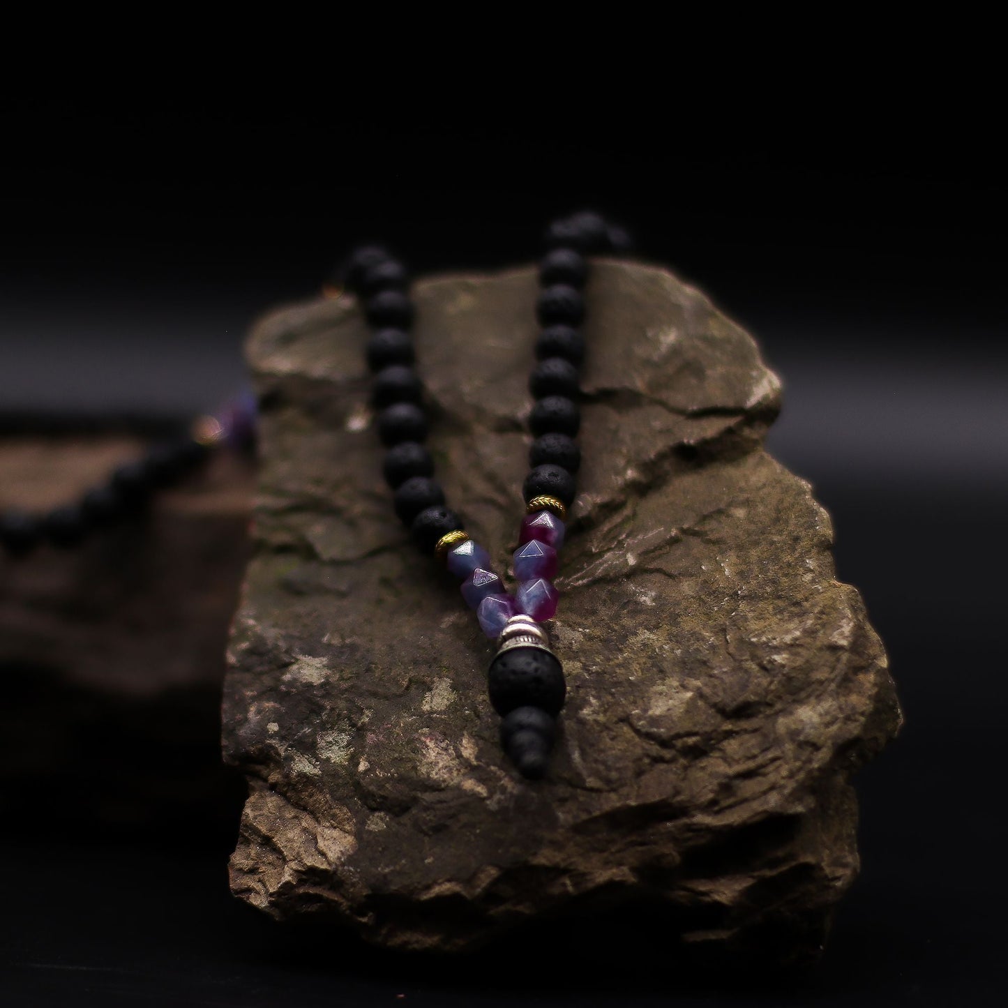 Volcanic & Gemstone Necklace – Embrace Dark Side on rock display, black lava stone beads with purple gemstone accent