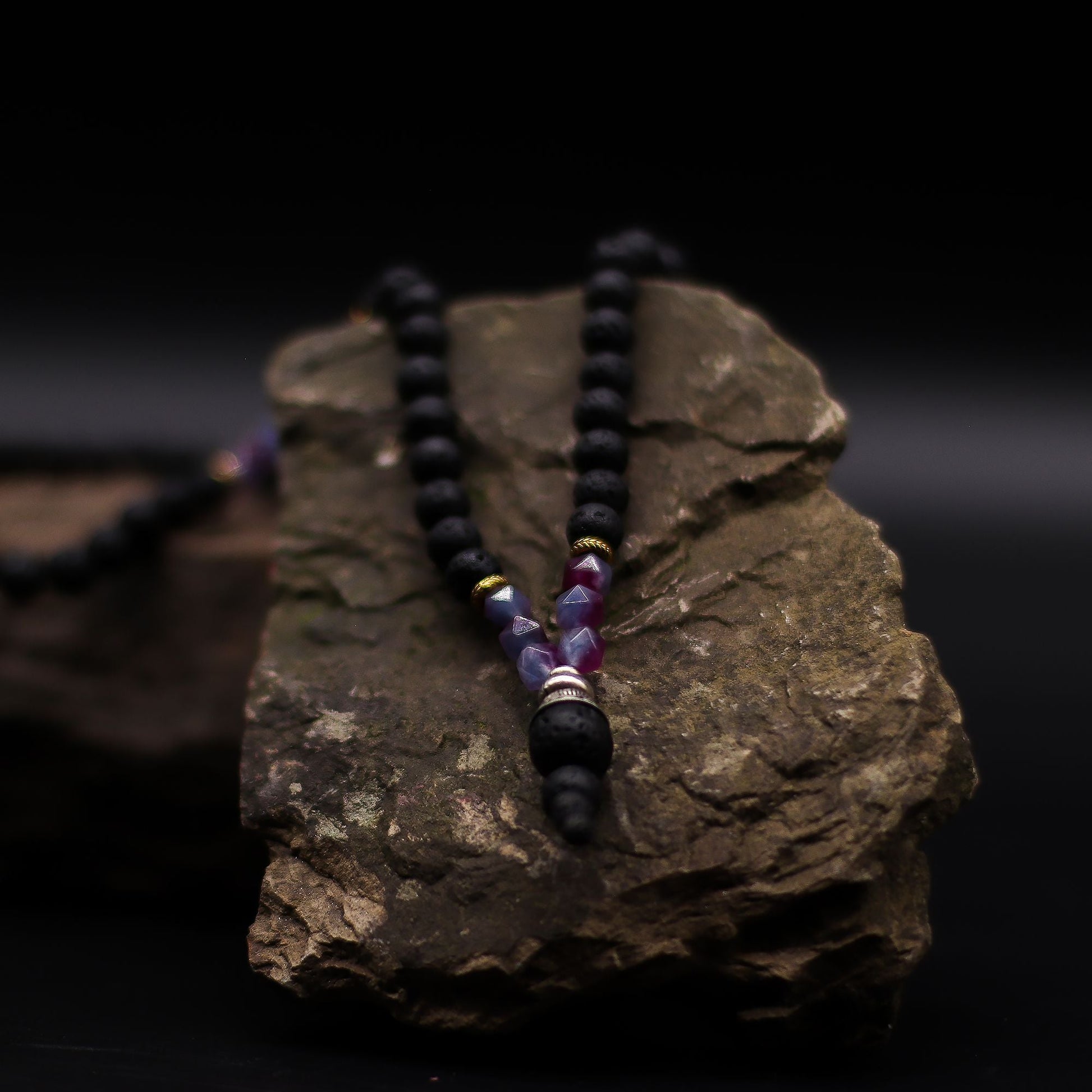 Volcanic & Gemstone Necklace – Embrace Dark Side on rock display, black lava stone beads with purple gemstone accent