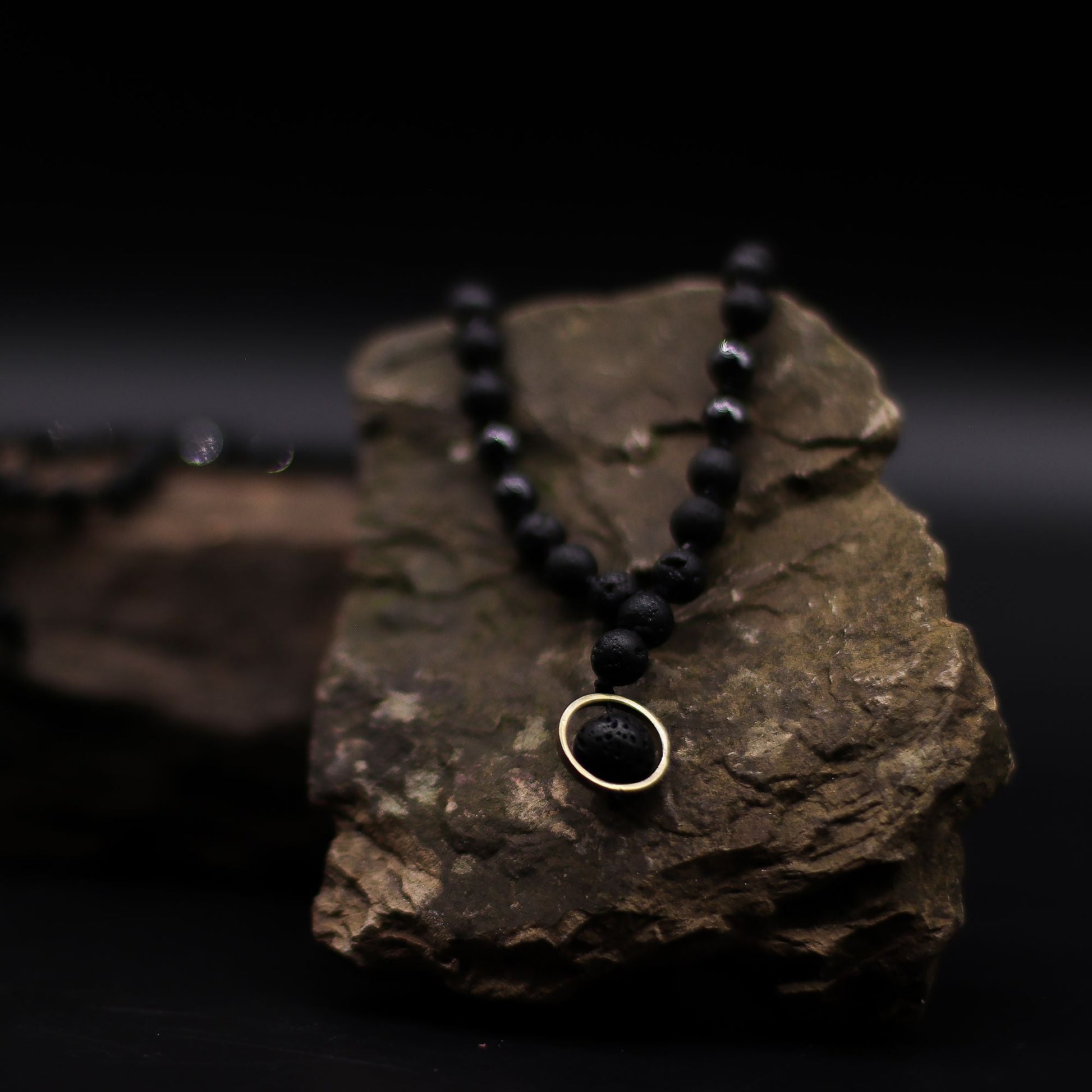 Halsband med vulkanisk lavasten – Renewal & Rebirth svart lavastenspärlhalsband med hänge med guldring på rock