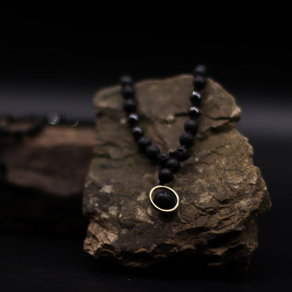 Halsband med vulkanisk lavasten – Renewal & Rebirth svart lavastenspärlhalsband med hänge med guldring på rock