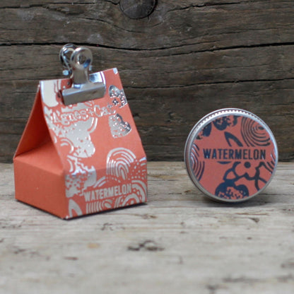 Alt Tag: Watermelon Vegan Lip Balm – 12G en lata, aroma a sandía, junto a caja de regalo roja sobre fondo de madera