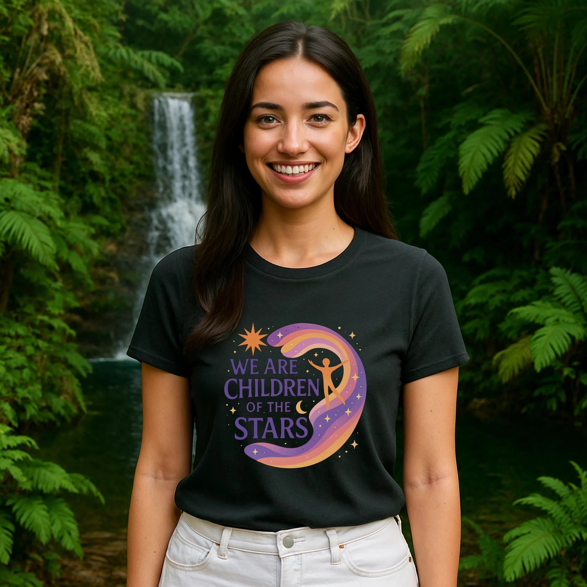 Model wearing We Are Children Of The Stars 100% Organic Cotton T-Shirt with cosmic graphic, outdoors near waterfall