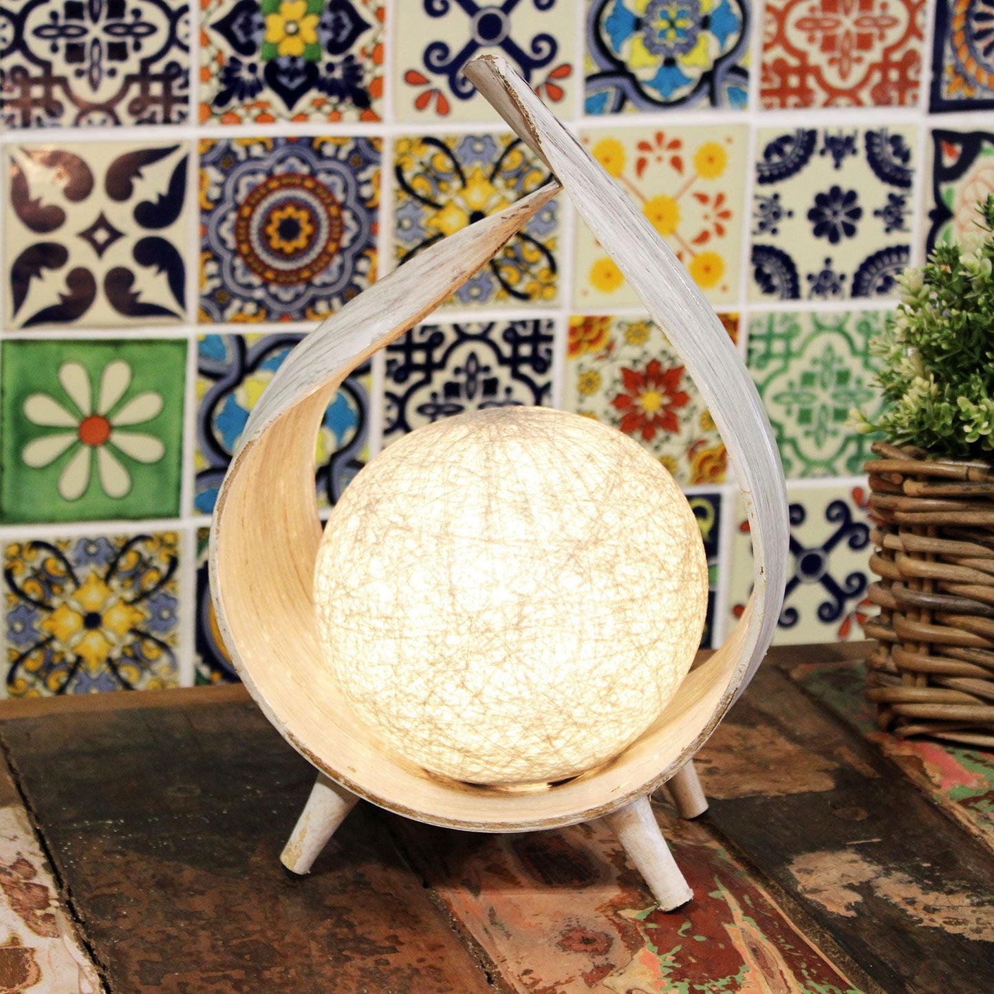 Alt Tag: Lámpara de Hoja de Coco Whitewash – Artesanía única, estructura de hoja de coco con acabado whitewash con globo de pantalla de algodón sobre mesa de madera