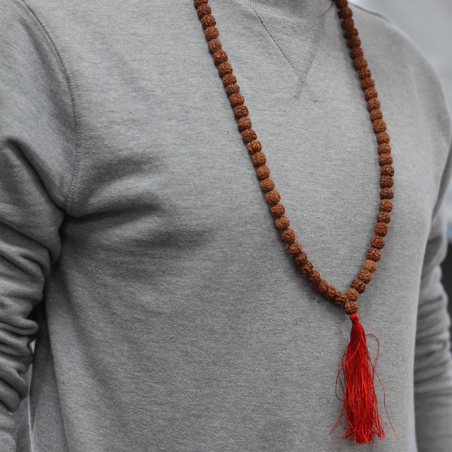 Alt Tag: Wood Bead Rudraksha Mala – 65 CM collar de cuentas Rudraksha marrones con borla roja, usado sobre sudadera gris