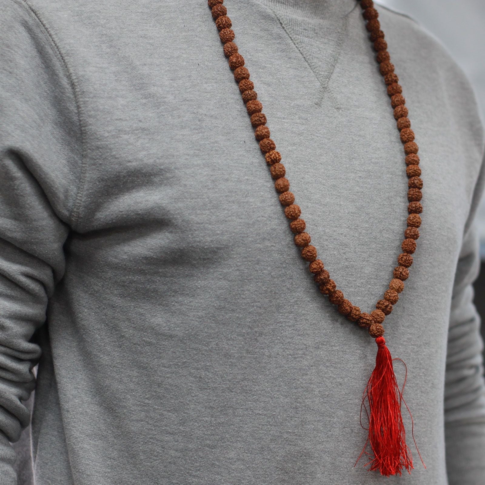 Alt Tag: Wood Bead Rudraksha Mala – 65 CM collar de cuentas Rudraksha marrones con borla roja, usado sobre sudadera gris