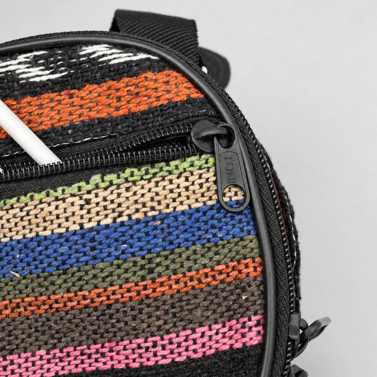 Close-up of the multicoloured woven front pocket, black zipper and a partially visible mallet shaft.