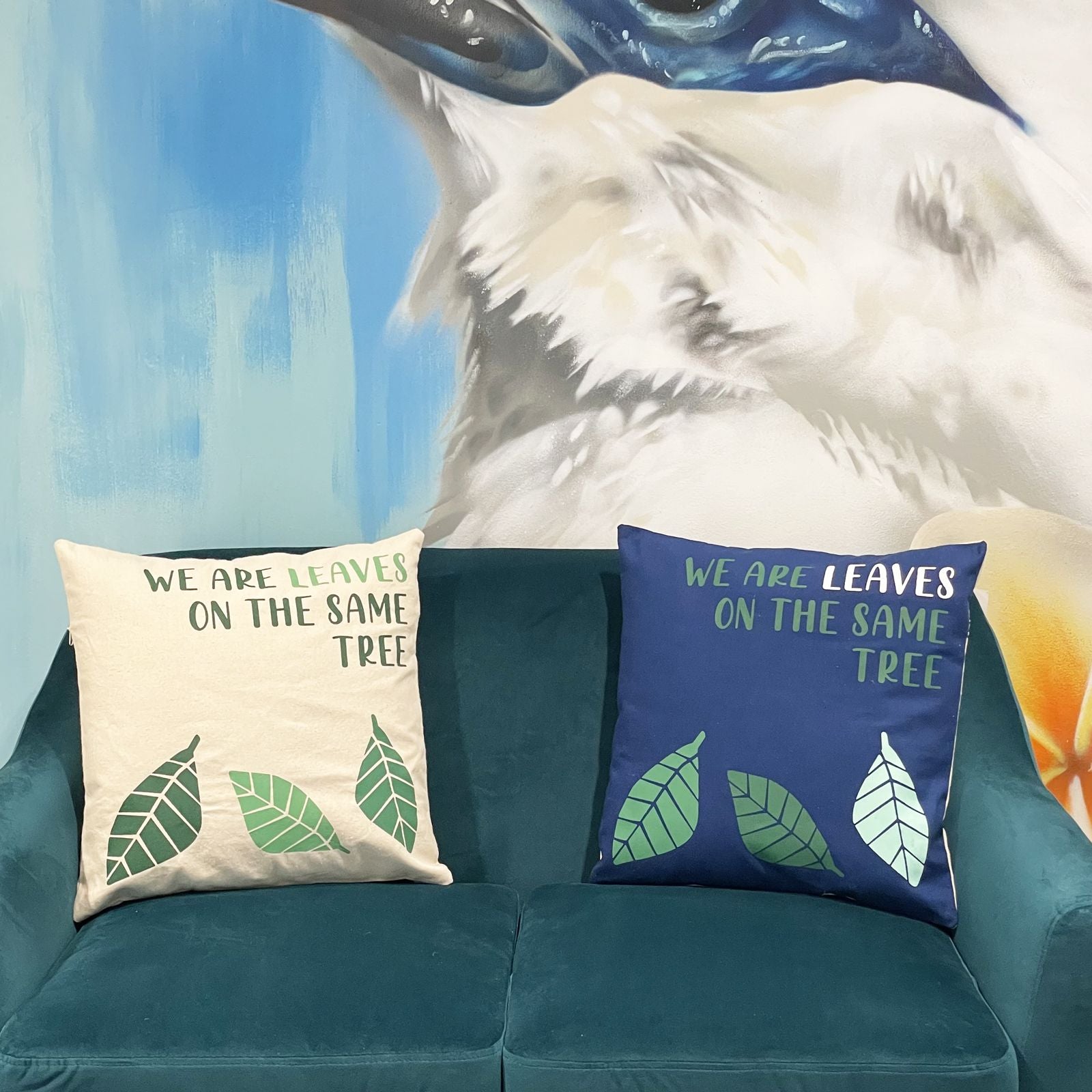 Alt Tag: Gult kuddfodral i bomull – 45x45 CM på soffa, gult bomullsfodral med bladtryck och citatet “We are leaves on the same tree”