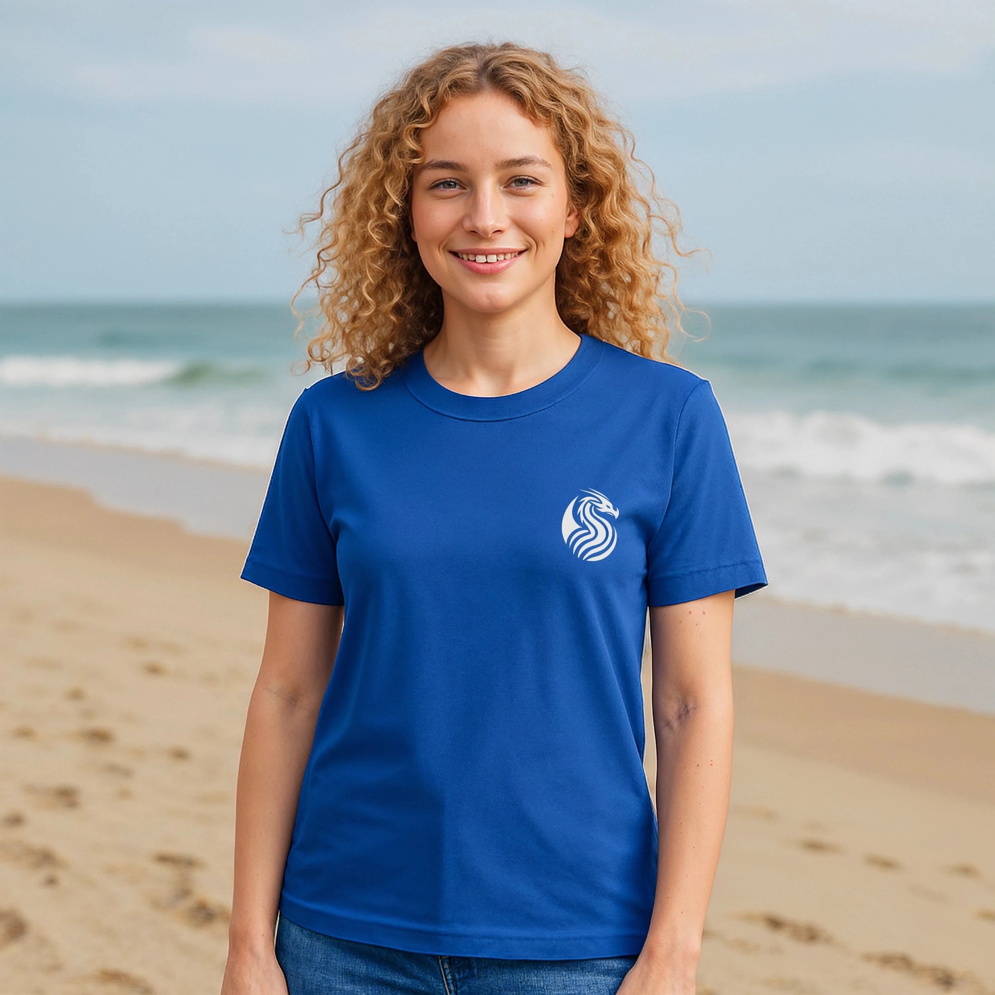 Alt Tag: Young Dragon Premium Unisex T-Shirt en azul, modelo sonriendo en la playa, logo de dragón blanco en el pecho